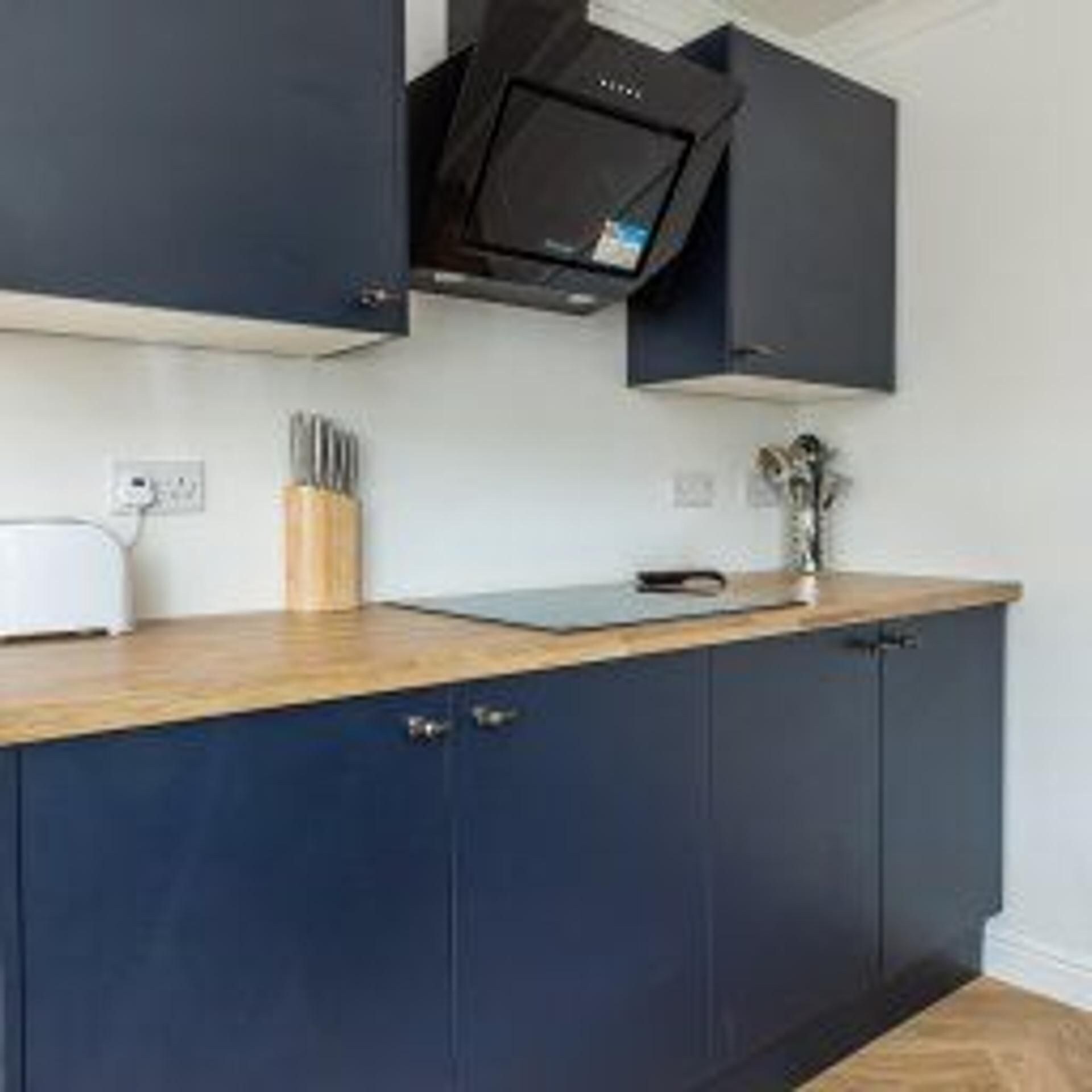 Una cocina con armarios azul oscuro, encimera de madera, microondas y un juego de cuchillos.