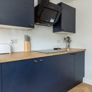Una cocina con armarios azul oscuro, encimera de madera, microondas y un juego de cuchillos.
