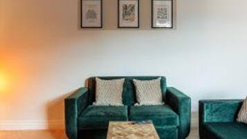 Una sala de estar con un sofá verde, una mesa de centro de madera y obras de arte enmarcadas en la pared.
