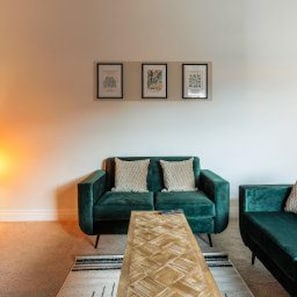 Una sala de estar con un sofá verde, una mesa de centro de madera y obras de arte enmarcadas en la pared.