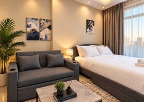 A modern hotel room with a grey sofa, a large bed, a coffee table with a book and a plant, and artwork on the walls. - VESTA - Luxury Studio - Hera tower (Dubai)