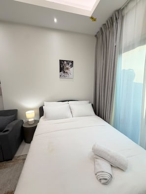 A hotel room with a bed, a nightstand, a lamp, a chair, and a window with curtains. - VESTA - Luxury Studio - Hera tower (Dubai)