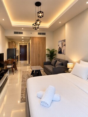 A modern hotel room with a bed, a seating area with a sofa and a table, a television, and a kitchenette. - VESTA - Luxury Studio - Hera tower (Dubai)