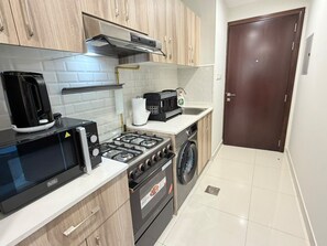 A compact kitchen with a microwave, stove, and washing machine. - VESTA - Luxury Studio - Hera tower (Dubai)