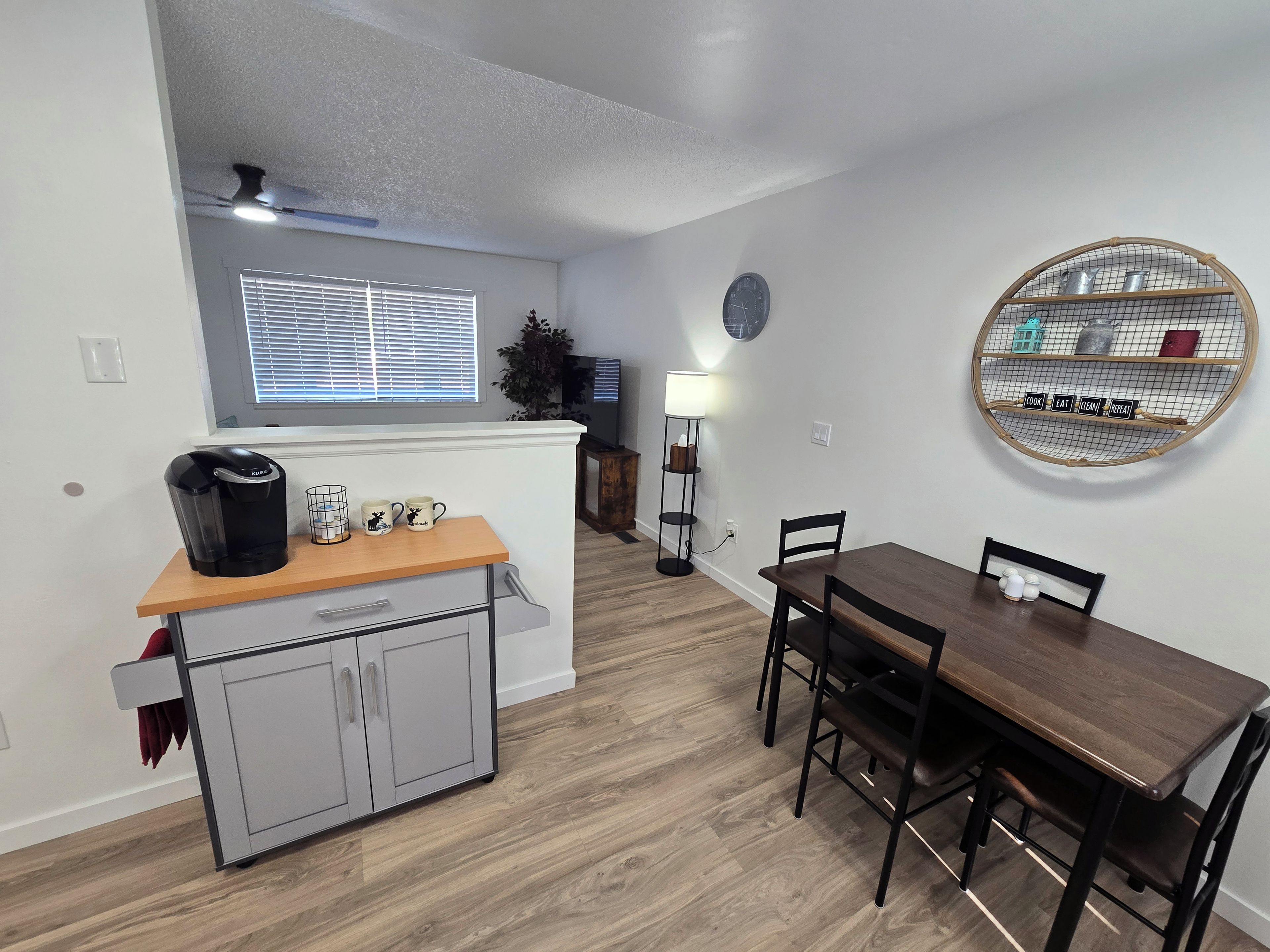 Een moderne keuken met een koffiezetapparaat, een eettafel met stoelen, een wandplank en een klok.