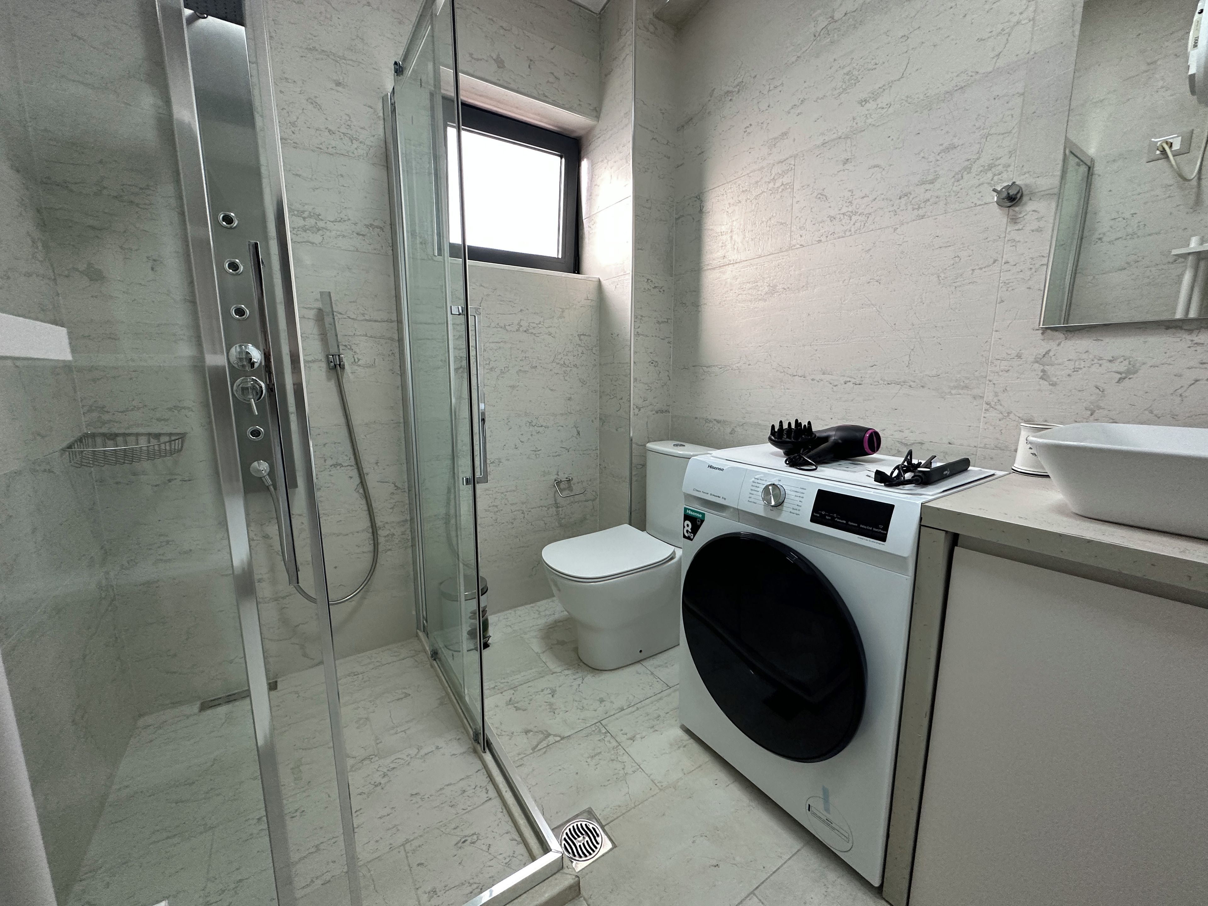 Un baño moderno con ducha envuelta en vidrio, inodoro y lavadora.