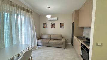A compact living space with a dining table, sofa, kitchenette, and a ceiling light fixture.