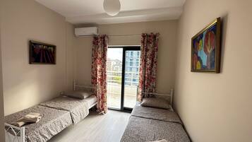 A room with two beds, a ceiling fan, a window with curtains, and a painting on the wall.