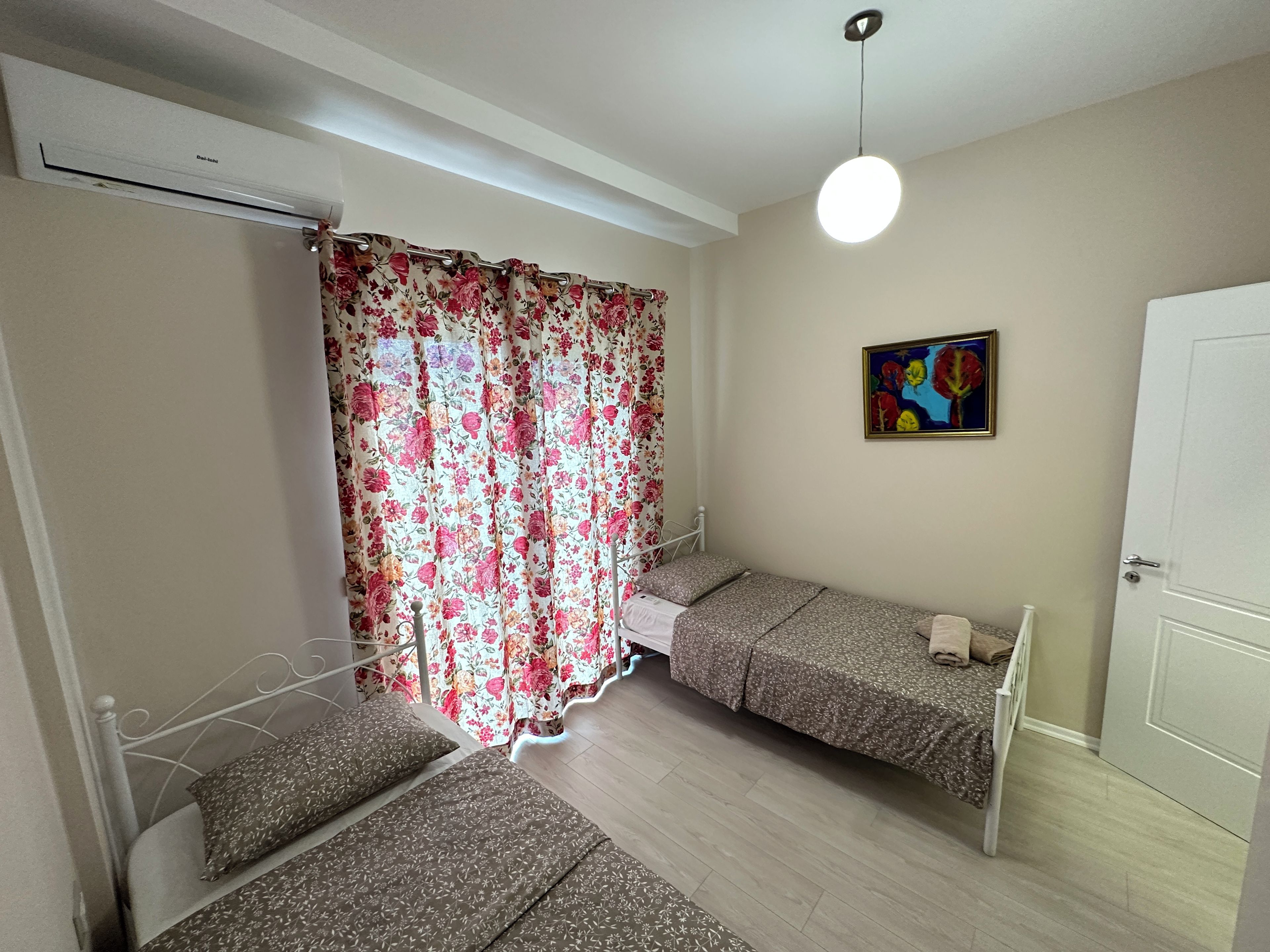 A room with two beds, a ceiling fan, a painting, and a door.