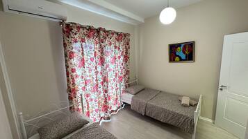 A room with two beds, a ceiling fan, a painting, and a door.