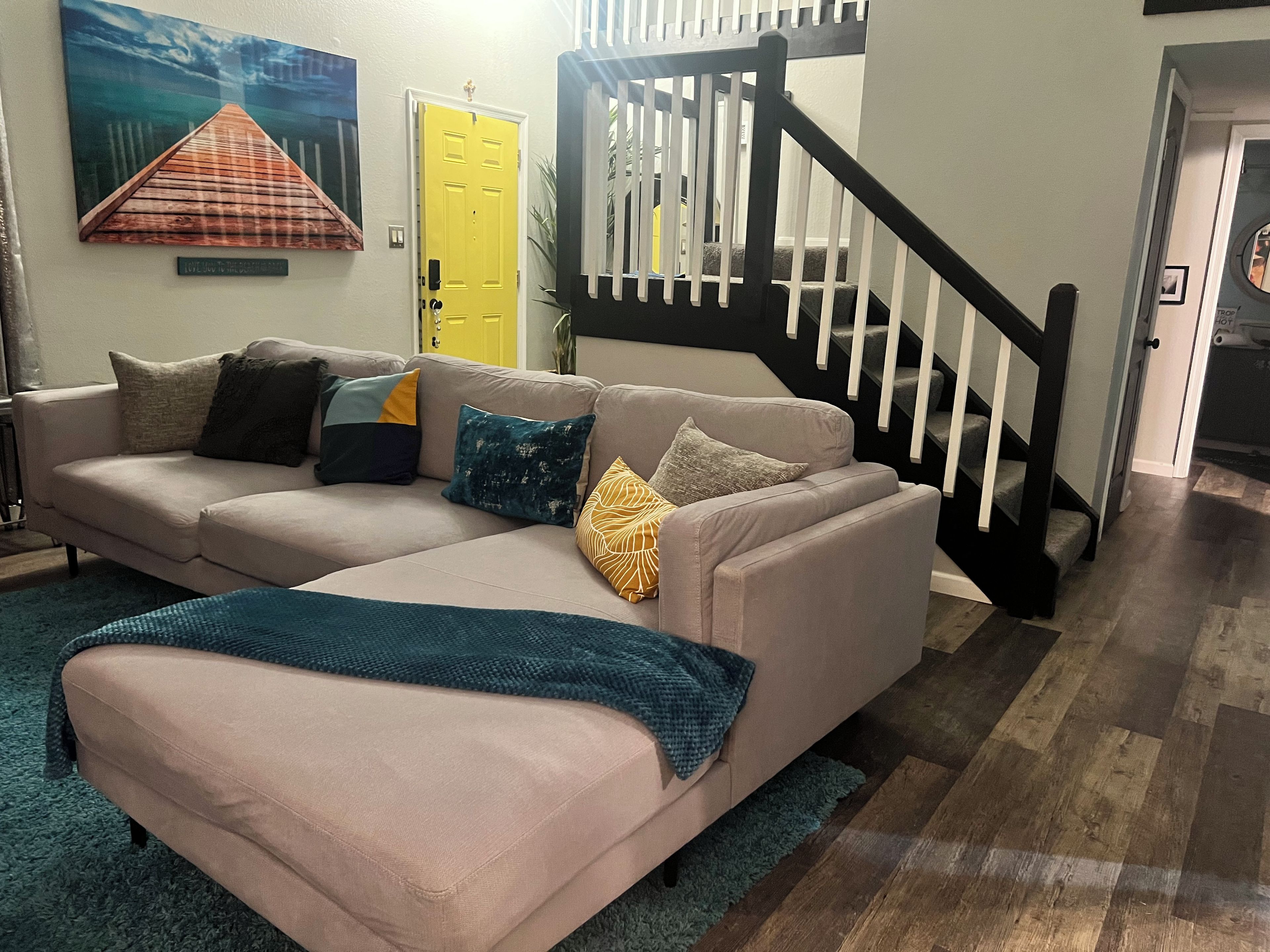 A living room with a beige sectional sofa, a blue throw blanket, and a yellow door.