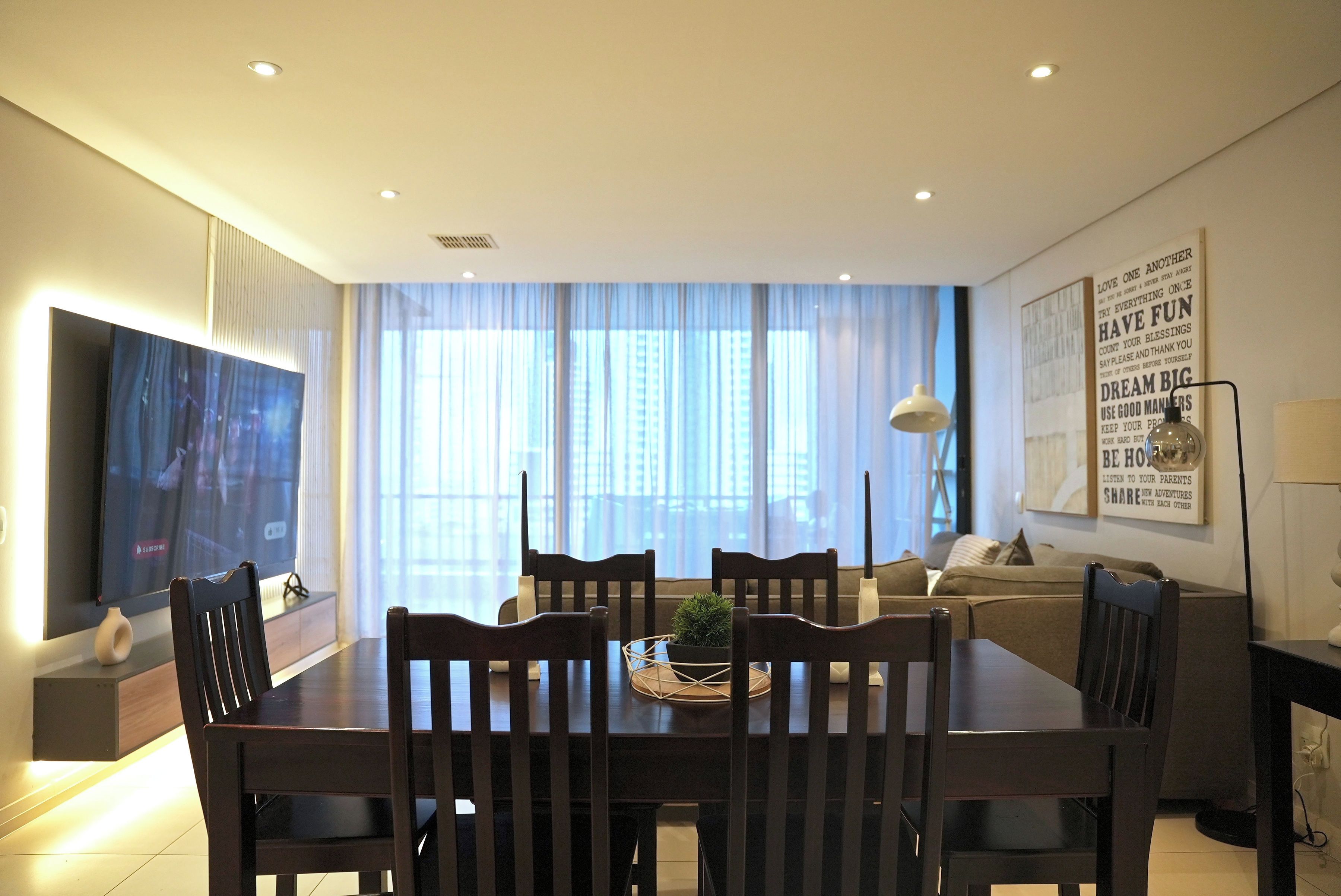 A modern living room with a dining table, chairs, a sofa, a TV, and a window with curtains.