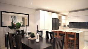 A modern kitchen with white cabinets, a black refrigerator, and a dining area with a dark wooden table and chairs. - 2-bedroom apartment in charming Durban with AC for relaxing stays (Durban)