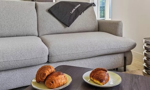 A grey sofa with a black throw blanket and two plates with croissants on a wooden table. - AN EXCEPTIONAL CENTRAL LOCATION FOR AN UNFORGETTABLE PARISIAN STAY-RUE DE RIVOLI (Paris)