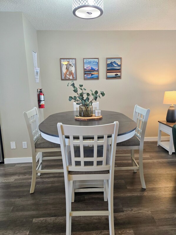 A dining area with a round table, white chairs, a vase with greenery, and three framed pictures on the wall. - Family & Pet Friendly 3BR, Large Fenced Yard- Close to South Health Campus (Calgary)