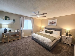 A bedroom with a bed, bedside tables, a ceiling fan, a window with curtains, and a wall-mounted picture. - Family & Pet Friendly 3BR, Large Fenced Yard- Close to South Health Campus (Calgary)