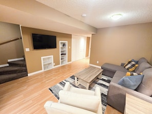 A living room with a sofa, coffee table, and TV. There are stairs leading to another room. - Family & Pet Friendly 3BR, Large Fenced Yard- Close to South Health Campus (Calgary)