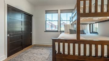 A room with a bunk bed, a dark wooden door, and a window with a view of houses.