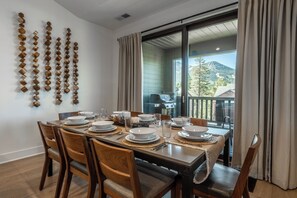 A dining area with a table set for four, wooden chairs, and a view of a mountain through a sliding glass door. - Beautiful CreekHouse with Amazing Views 322 (Mammoth Lakes)