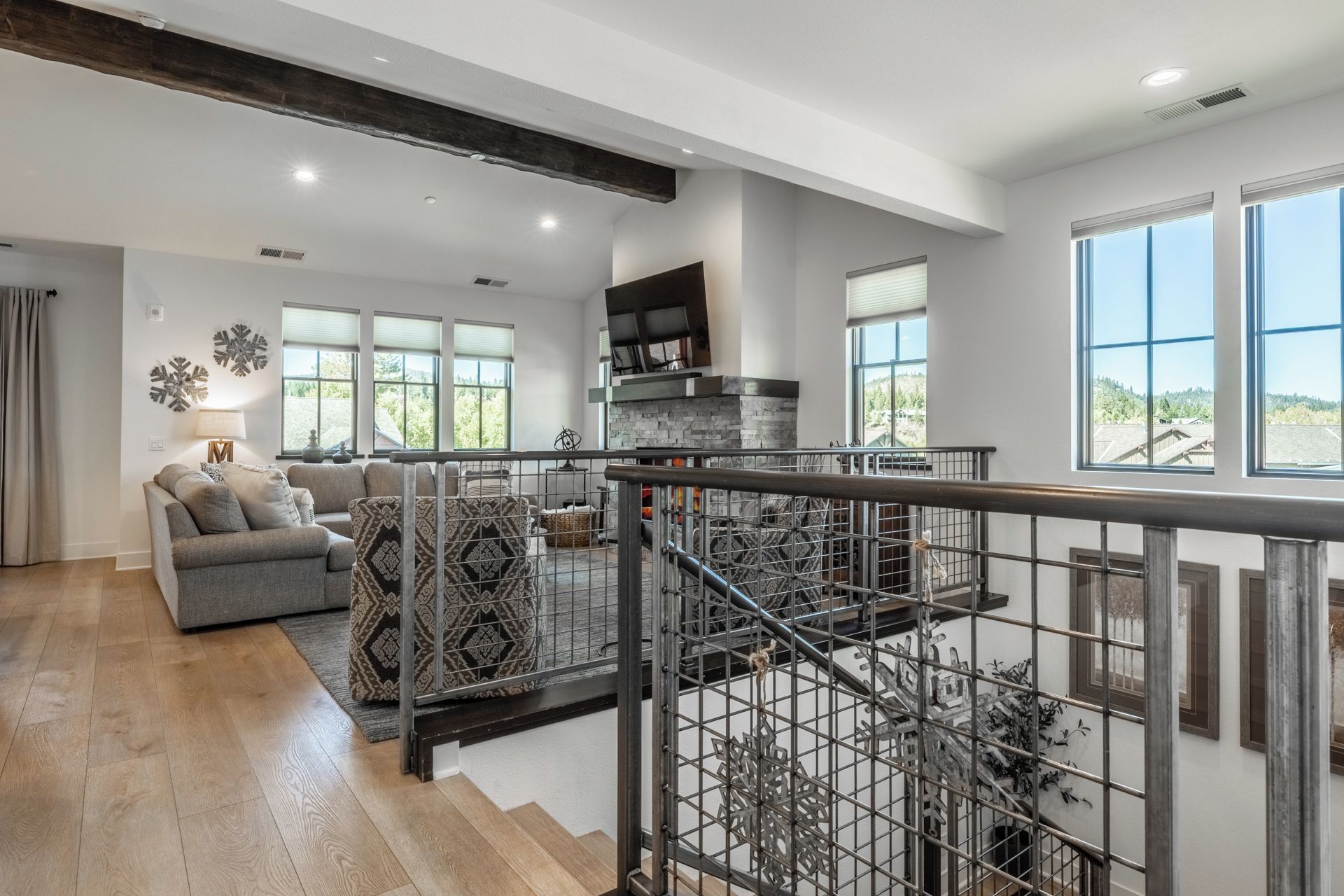 A spacious living area with a modern fireplace, a staircase with a metal railing, and large windows offering a view of the outdoors.