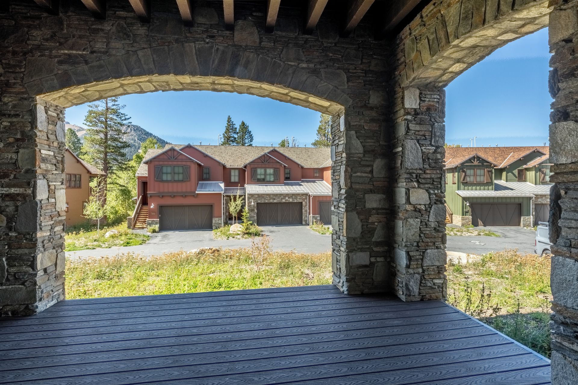 A stone archway leading to a residential area with houses and a clear sky.