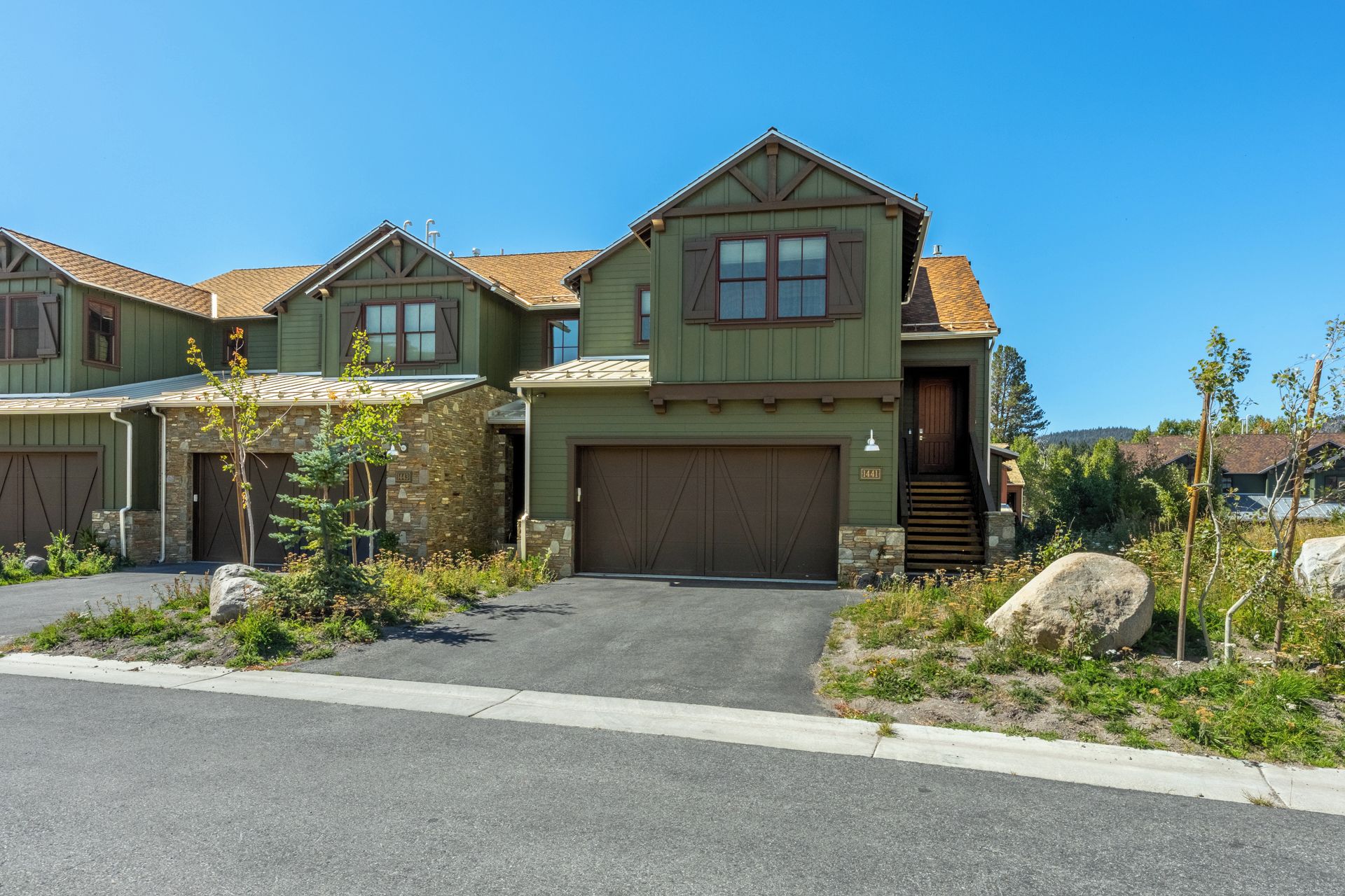 A two-story house with a garage, a stone foundation, and a well-maintained front yard with rocks and plants.