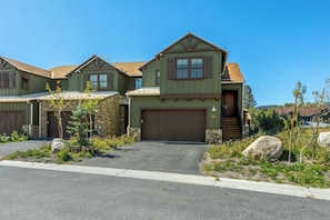 A two-story house with a garage, a stone foundation, and a well-maintained front yard with rocks and plants. - Beautiful CreekHouse with Amazing Views 322 (Mammoth Lakes)