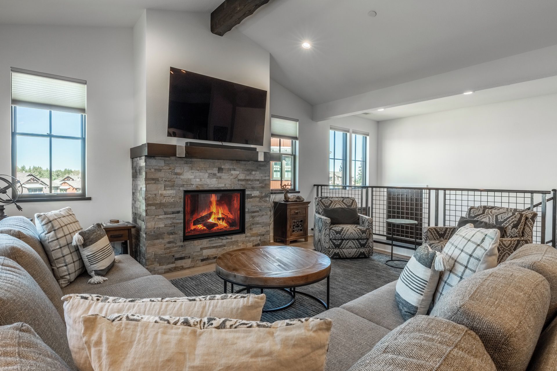 A living room with a stone fireplace, a television mounted above it, and a balcony with a railing.