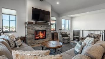 A living room with a stone fireplace, a television mounted above it, and a balcony with a railing.