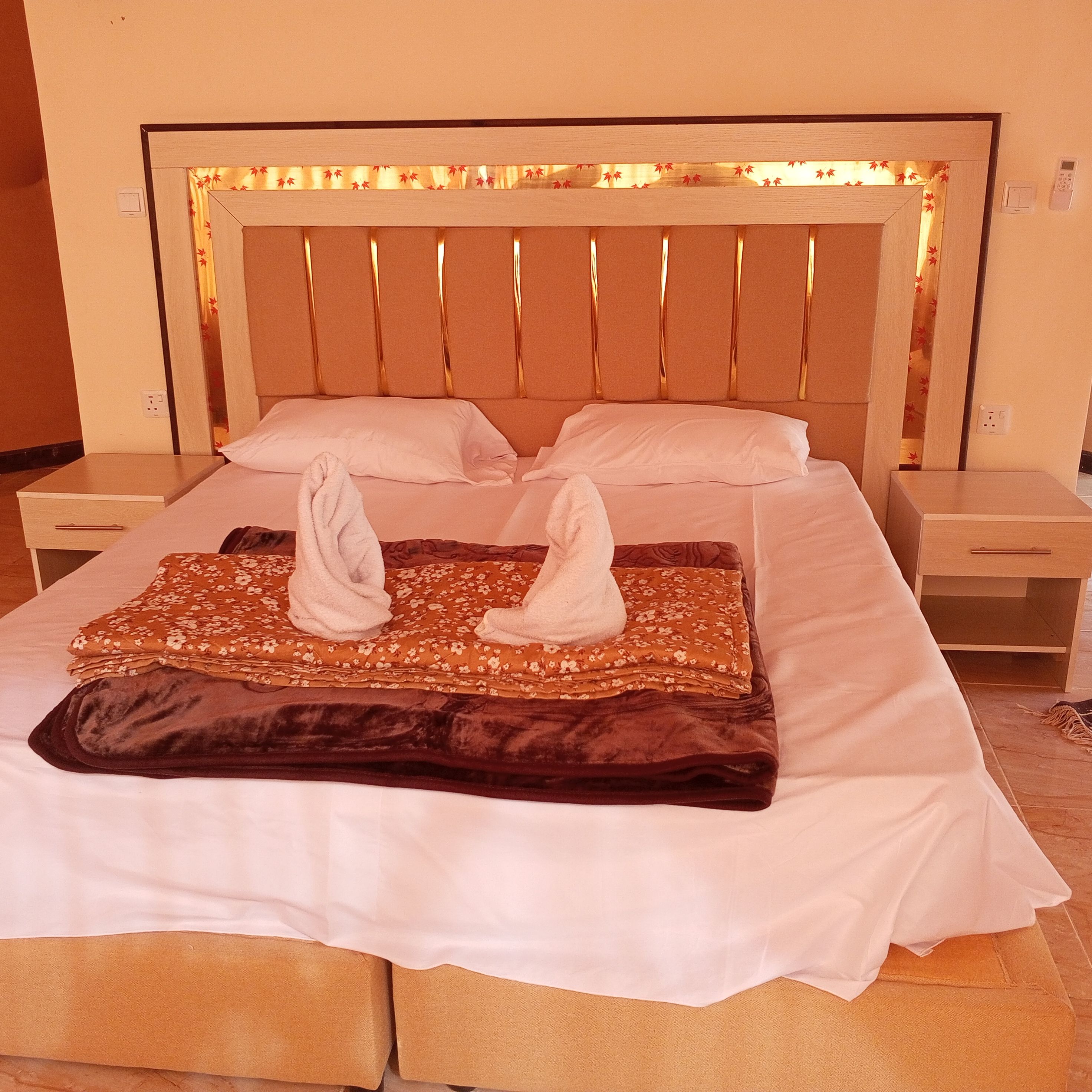 A neatly made bed with a headboard, two pillows, a folded blanket, and two towels.