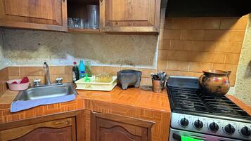 A kitchen with wooden cabinets, a sink, a stove, and various kitchen utensils.