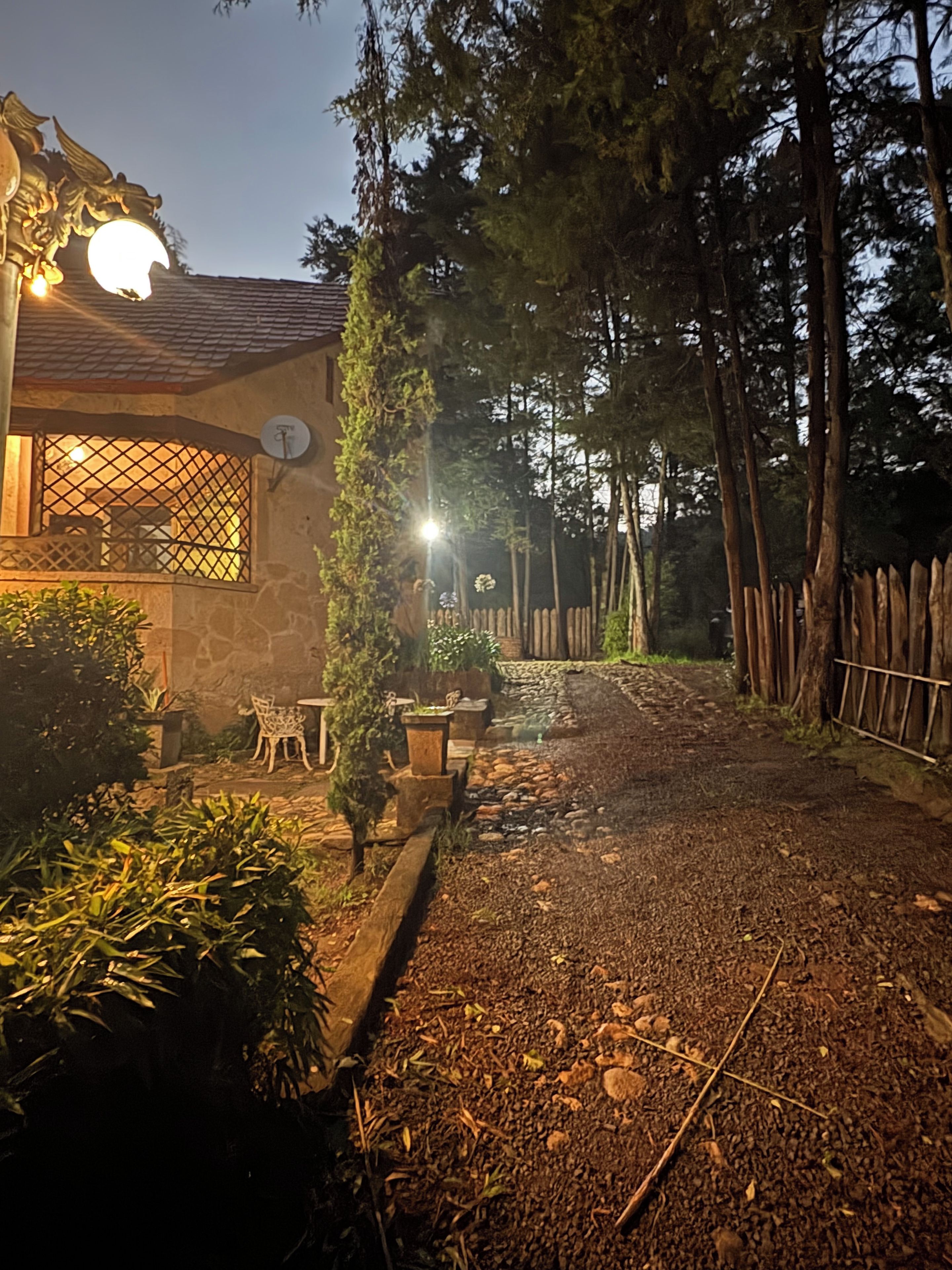 A pathway leading to a house with a stone facade, a satellite dish, and a fence.