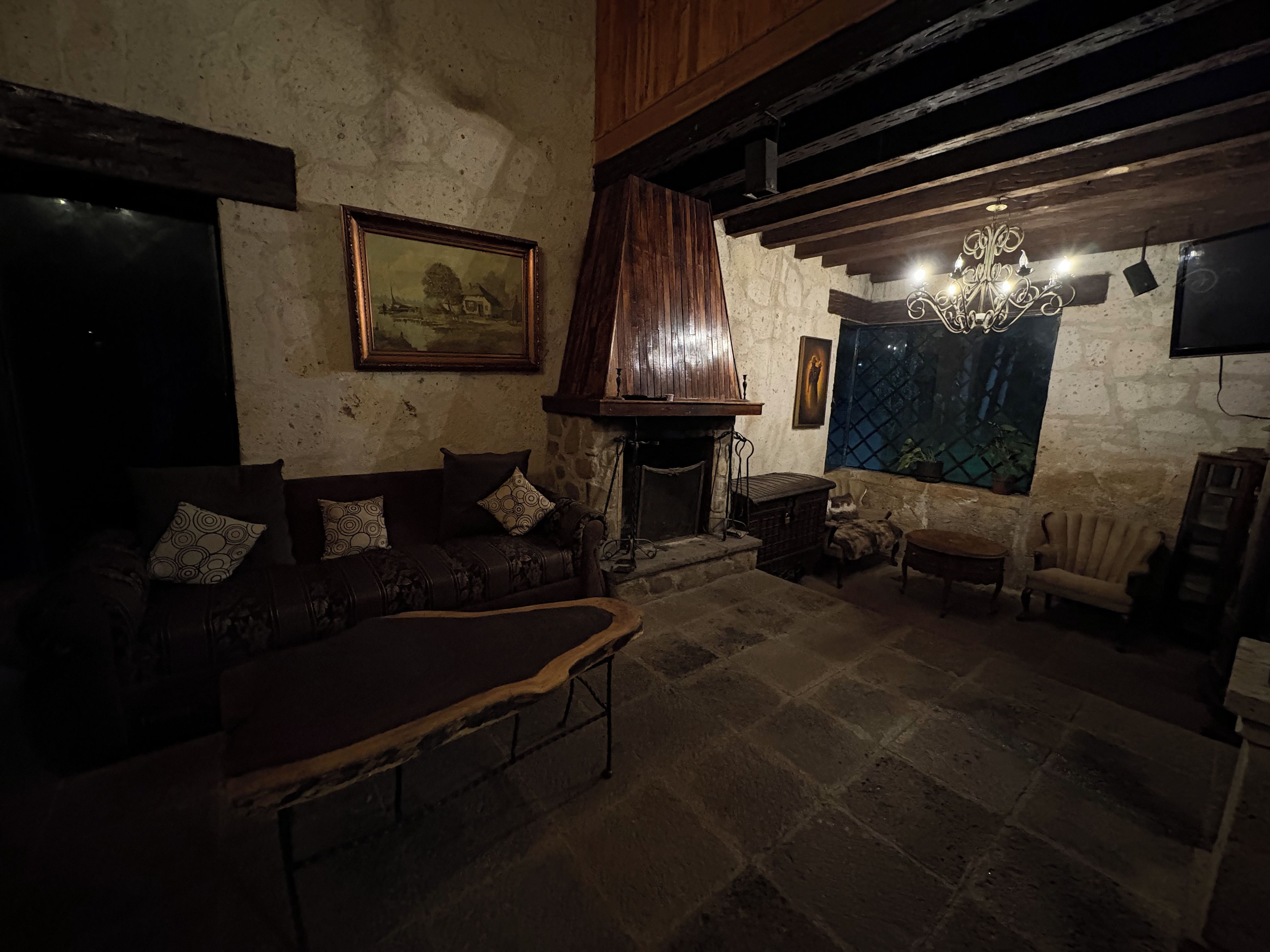 Un ambiente rustico con camino in pietra, travi in legno, un divano in pelle e una poltrona d'epoca.