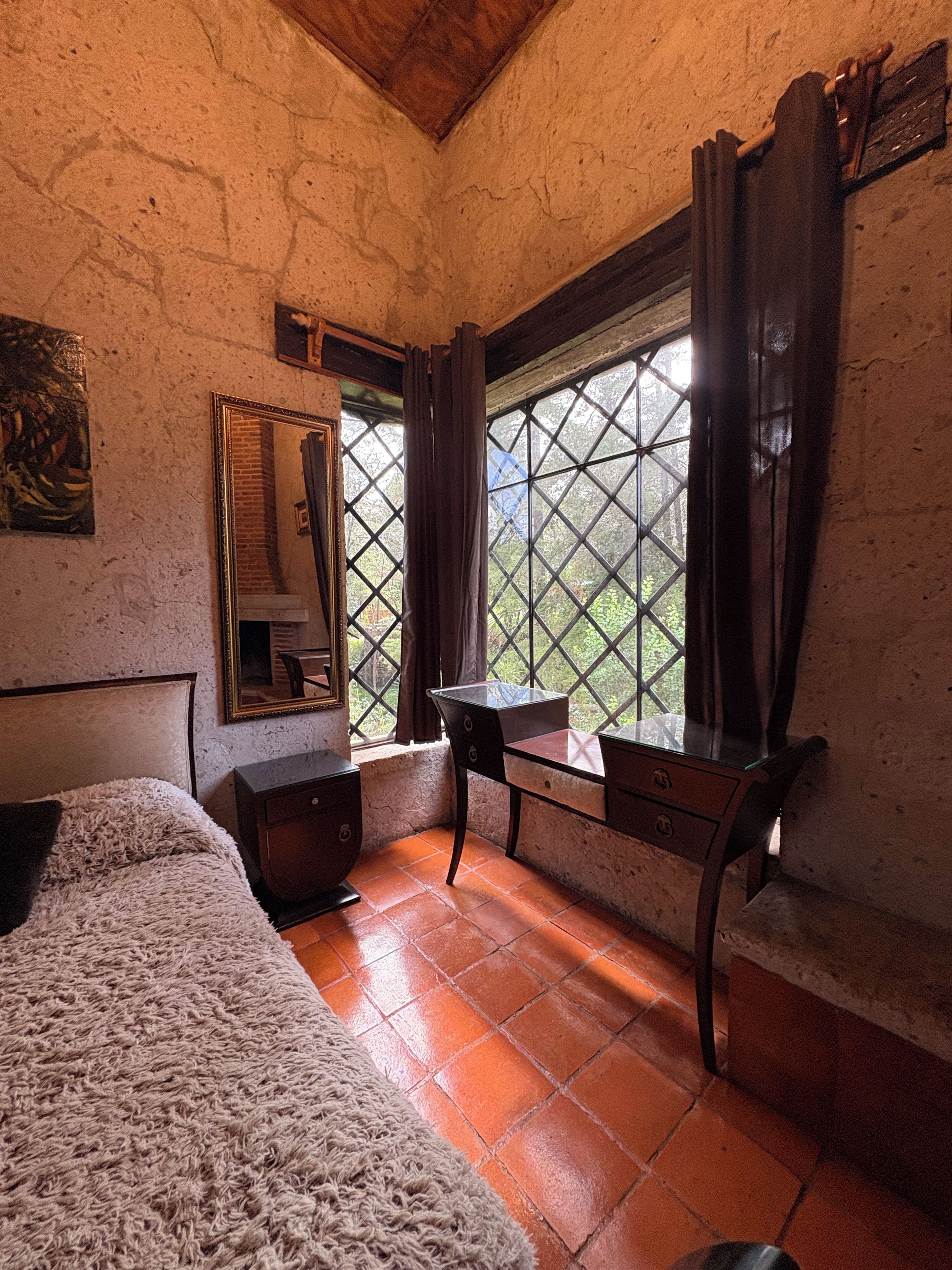A room with a bed, a desk, and a window with curtains.