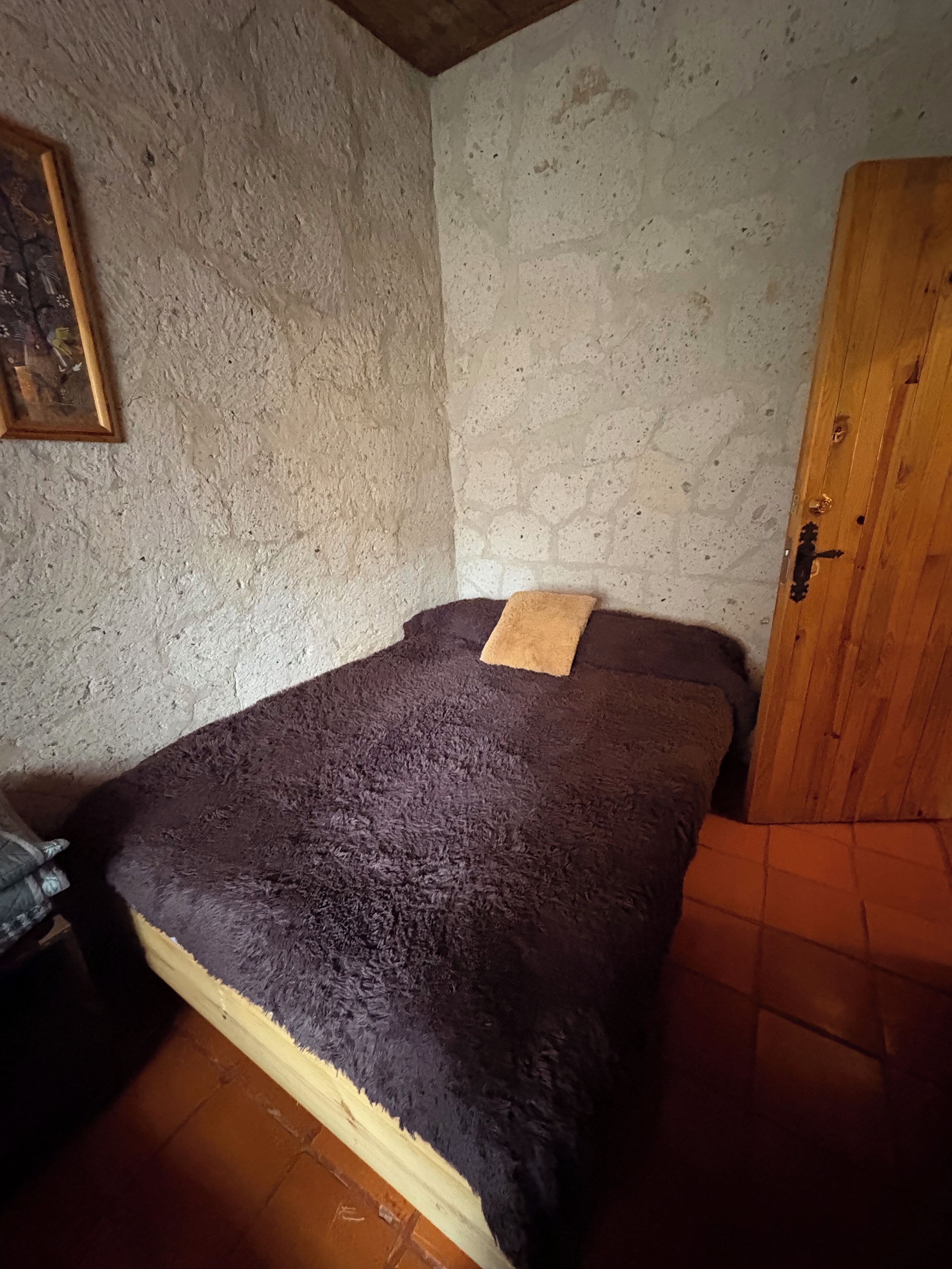A small, dimly lit room with a single bed, a wooden wardrobe, and a textured wall.