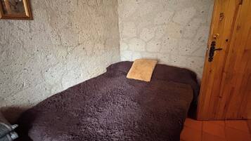 A small, dimly lit room with a single bed, a wooden wardrobe, and a textured wall.
