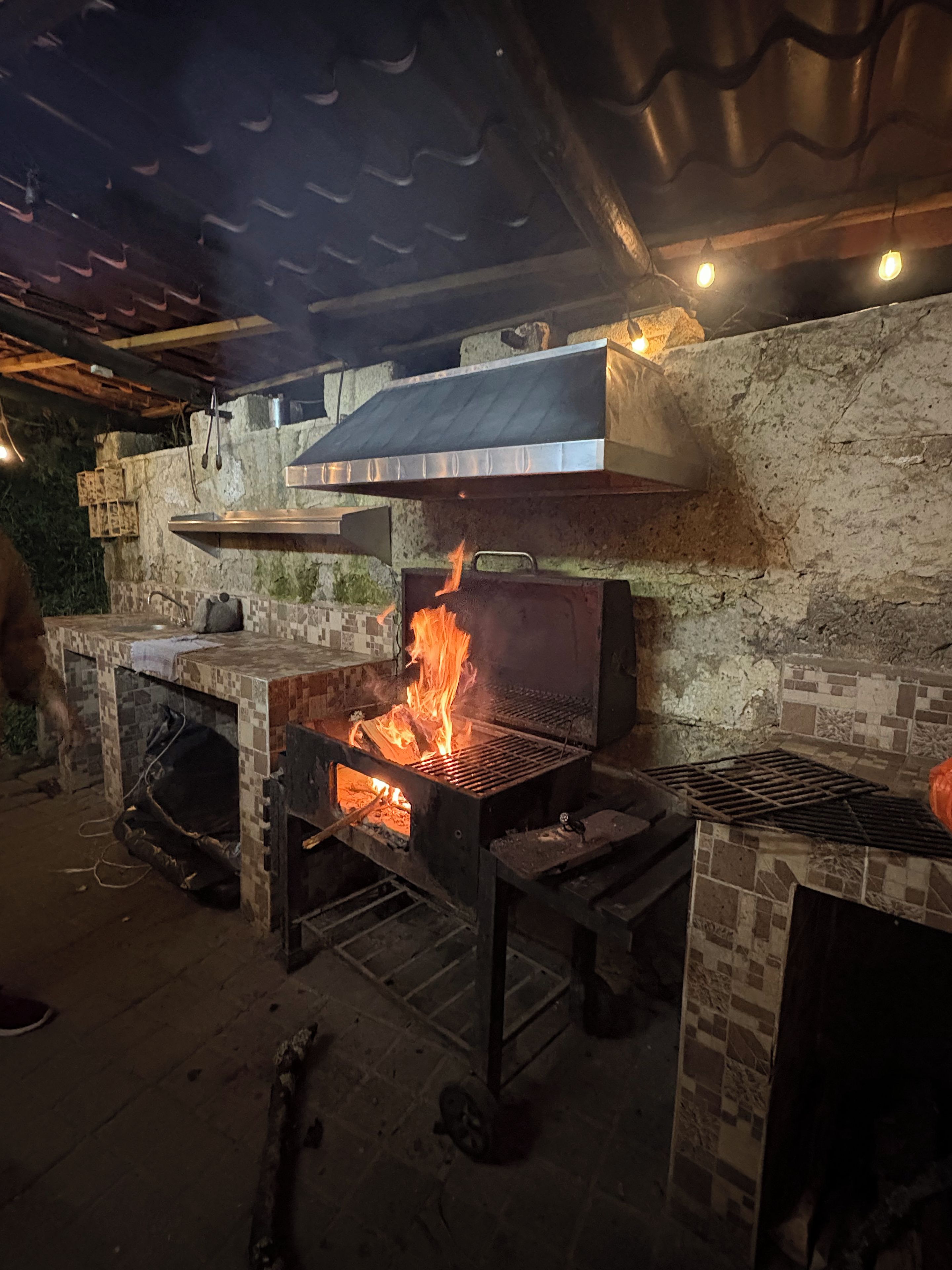 Un espace de cuisson extérieur doté d’un barbecue et d’un foyer, entouré de murs en pierre et doté d’un sol carrelé.