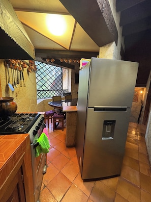 Een keuken met een gasfornuis, een koelkast en een eethoek met een tafel en stoelen.