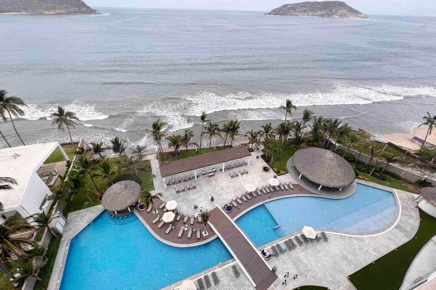 A resort with a large swimming pool, lounge areas, and a view of the ocean.