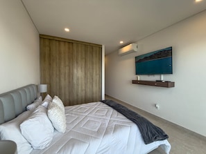 Ein modernes Schlafzimmer mit einem Bett, einem Holzschrank, einem an der Wand befestigten Fernseher und einer Klimaanlage.