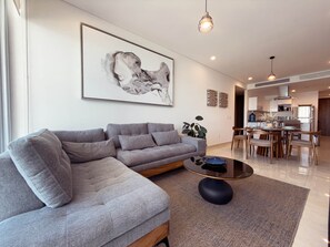 Ein modernes Wohnzimmer mit einem grauen Ecksofa, einem runden Couchtisch und einem großen abstrakten Gemälde an der Wand.