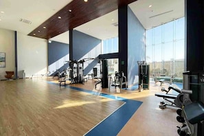 Ein geräumiger Fitnessraum mit verschiedenen Trainingsgeräten, großen Fenstern und Holzboden.