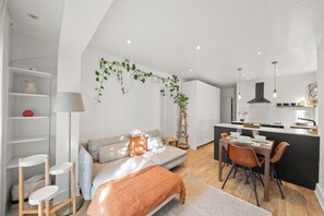 A modern living space with a sofa, dining table, and chairs, a kitchen area with a black countertop, and a staircase leading to an upper level. - Bright 2 bed Chiswick by ARP Homes l 5 min tube & Heathrow (Greater London)