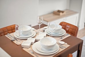 A dining table set with white plates, bowls, and cutlery, with a wine glass and a box in the background. - Bright 2 bed Chiswick by ARP Homes l 5 min tube & Heathrow (Greater London)