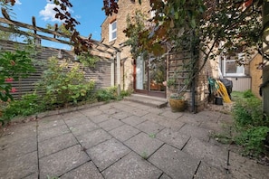 A paved courtyard with a wooden fence, a brick wall, and a door leading to a building. - Bright 2 bed Chiswick by ARP Homes l 5 min tube & Heathrow (Greater London)