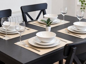 Ein Esszimmertisch mit weißen Tellern, Schüsseln und Weingläsern, zusammen mit einem kleinen Topfpflanzen.