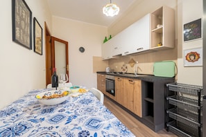 A compact kitchen with wooden cabinets, a dining table with a blue patterned tablecloth, and a bowl of walnuts. - ElleEsse Apartment: Between Ortigia and the Archaeological Park. Two bathrooms, large living room (Siracusa)