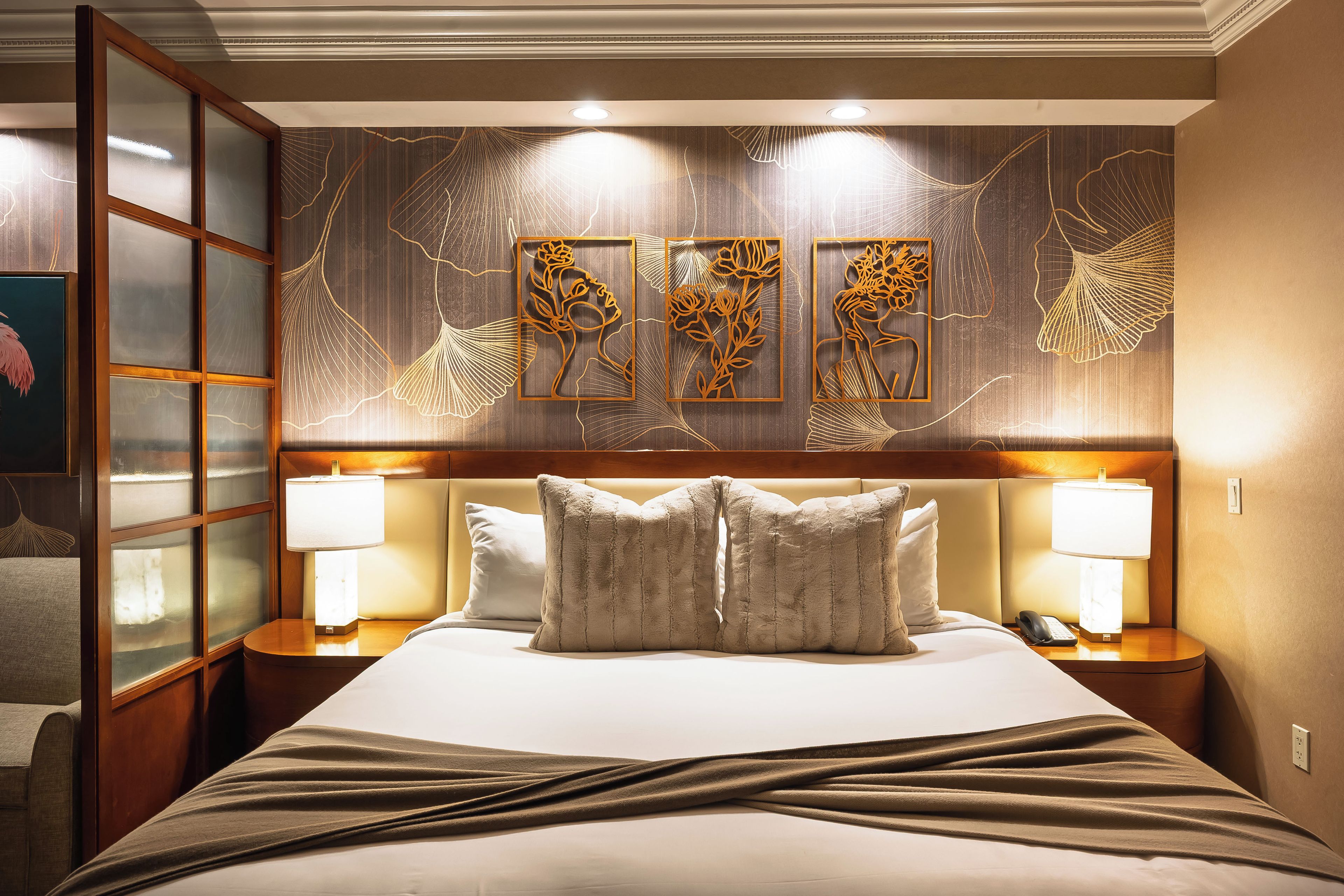 A hotel room with a large bed, two bedside lamps, a headboard with a floral design, and a wall with three framed artworks.