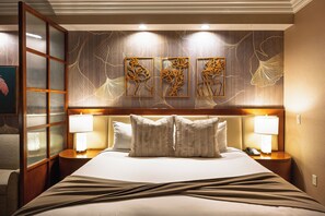 Una habitación de hotel con una cama grande, dos lámparas de noche, un cabecero con diseño floral y una pared con tres cuadros enmarcados.