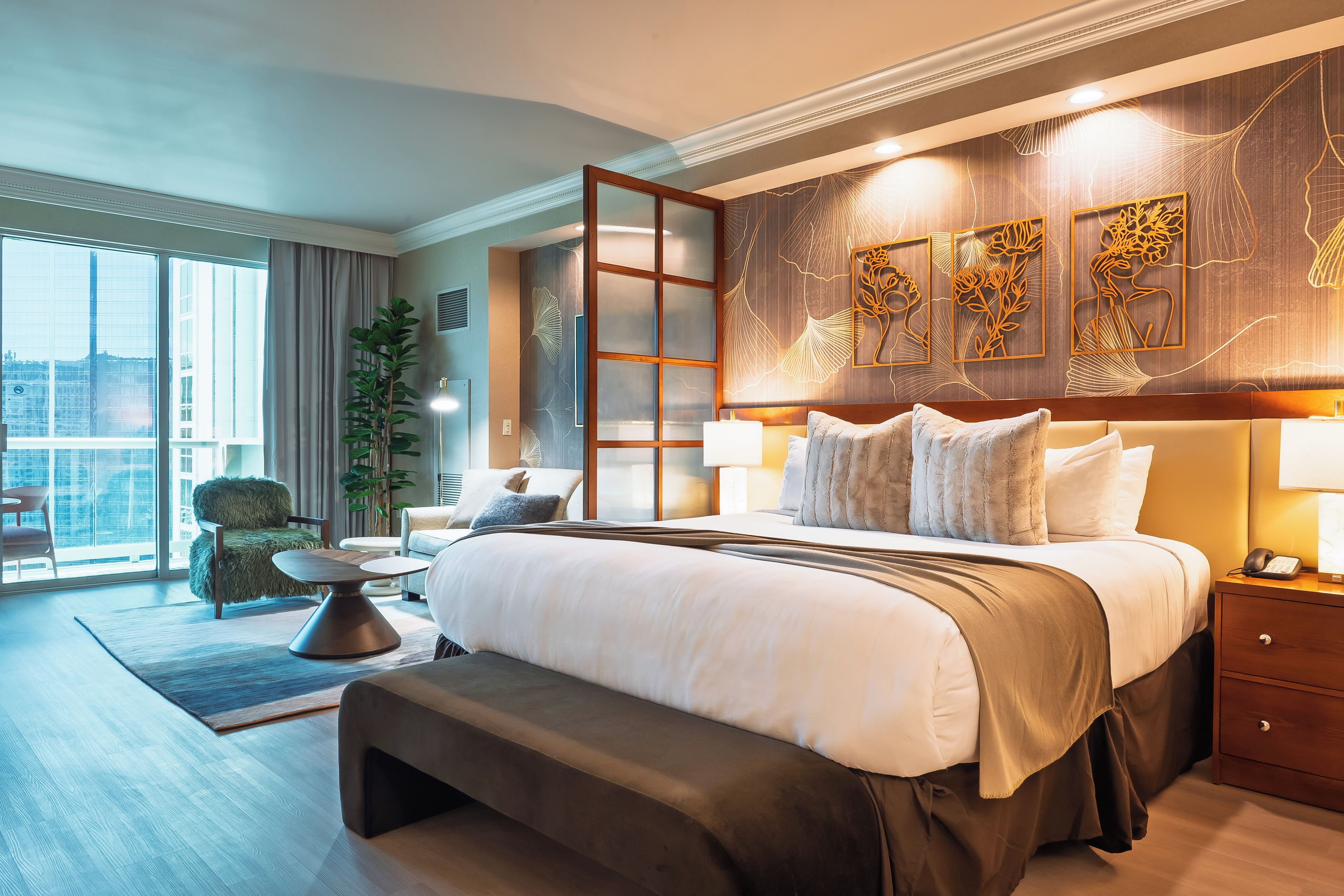 A modern hotel room with a large bed, bedside tables, a desk, and a view of the city.